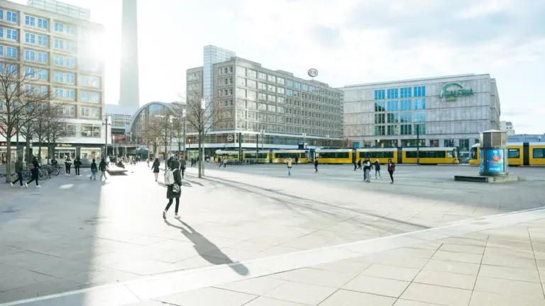 Der Berliner Alexanderplatz mit Straßenbahn und umliegenden modernen Gebäuden bei Tageslicht.