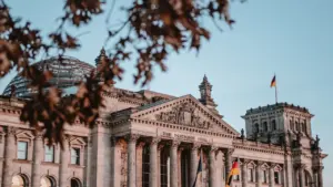 Das Reichstagsgebäude in Berlin unter blauem Himmel mit deutscher Flagge im Vordergrund.
