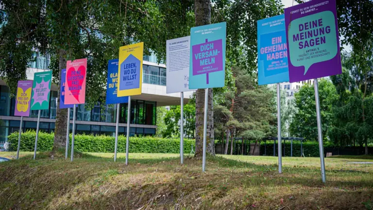 Bunte Informationstafeln in einem Berliner Park, die zur politischen Meinungsäußerung und Teilhabe aufrufen.