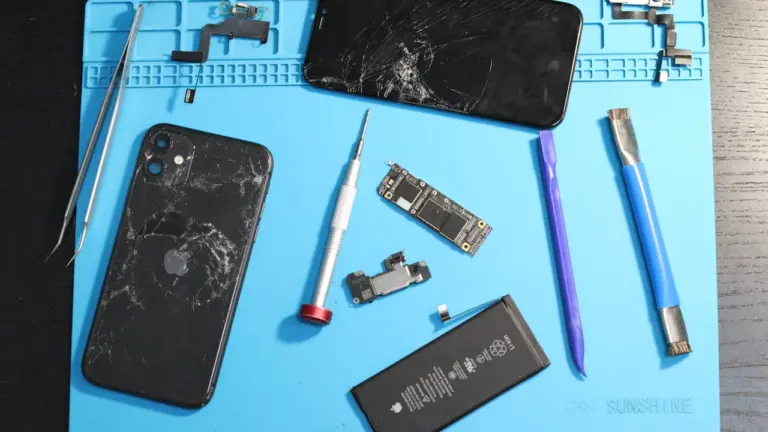 Ein zerlegtes Smartphone und diverse Reparaturwerkzeuge liegen auf einer blauen Arbeitsmatte bereit.