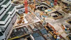 Luftaufnahme einer großen Baustelle mit Kränen und modernen Bürogebäuden in der Stadt.