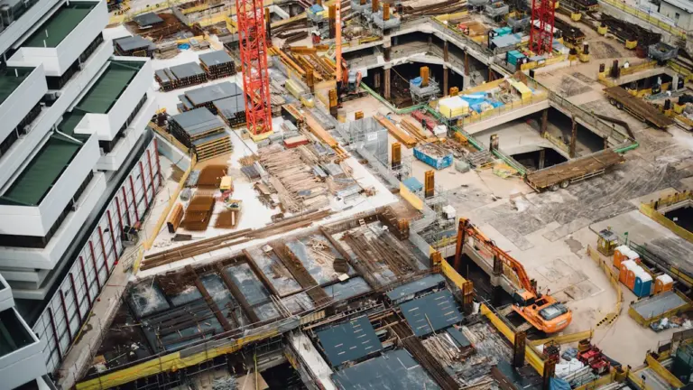 Luftaufnahme einer großen Baustelle mit Kränen und modernen Bürogebäuden in der Stadt.