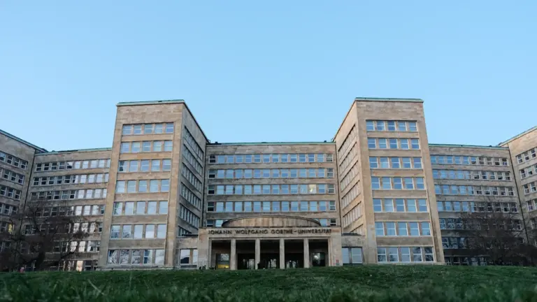 Die Goethe-Universität in Frankfurt am Main an einem sonnigen Tag mit grüner Wiese.