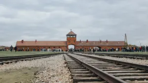 Die Gleise vor dem Eingangstor der Gedenkstätte Auschwitz-Birkenau unter bewölktem Himmel.