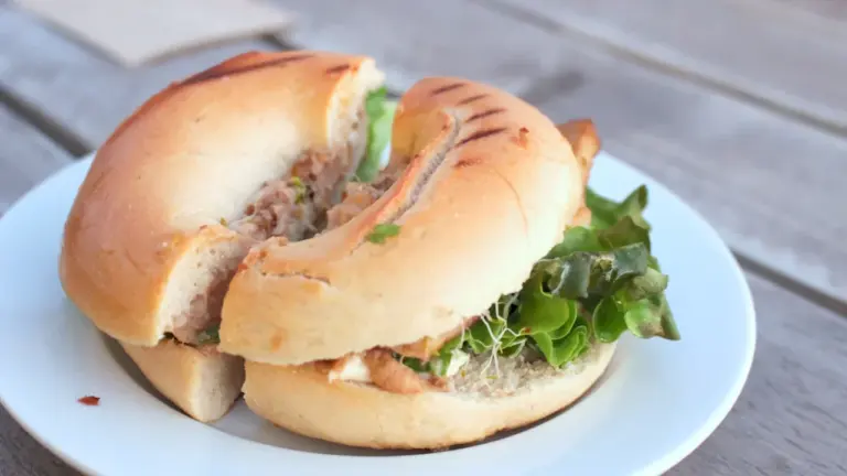 Ein belegtes Bagel-Sandwich auf einem weißen Teller als Symbol für gesundes Pausenbrot.