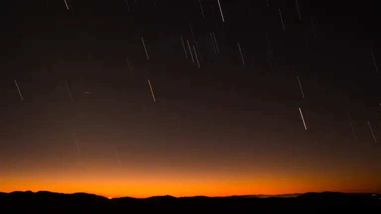 Sternschnuppen am dunklen Nachthimmel über einer silhouettierten Hügelkette während einer klaren Nacht.