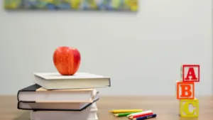 Ein roter Apfel auf einem Stapel Schulbücher neben ABC-Bausteinen und Buntstiften auf einem Tisch.