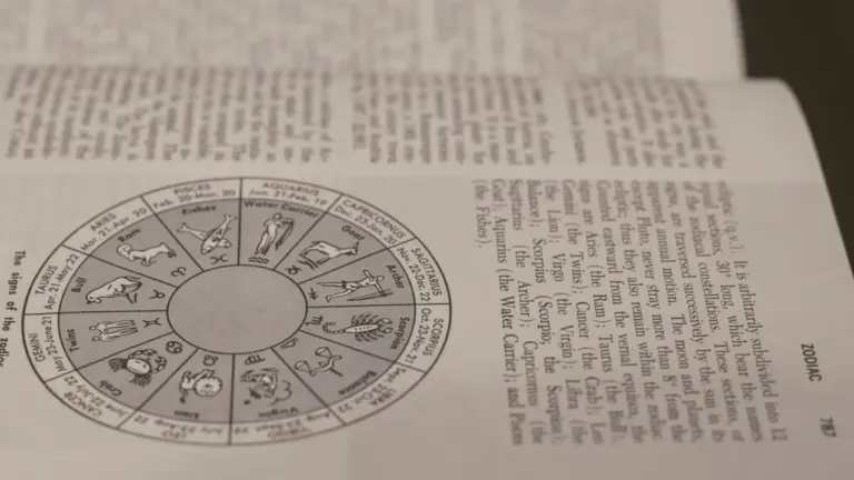 Ein offenes Buch mit astrologischen Symbolen und Tierkreiszeichen auf einer hellen Unterlage.