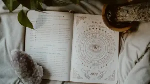 Ein offenes Tagebuch mit astrologischen Zeichnungen, Kristallen und einer Pflanze auf einem Bett.