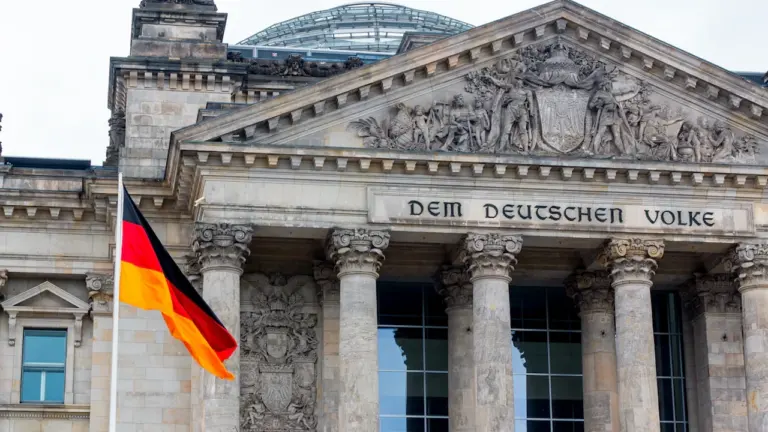 Das Reichstagsgebäude mit der deutschen Flagge unter einem hellblauen Himmel in Berlin.