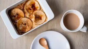 Apfel-Hafer-Auflauf in einer Auflaufform mit Tasse Kaffee auf einem Holztisch.