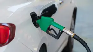 Eine Zapfpistole beim Betanken eines weißen Autos an einer Tankstelle.