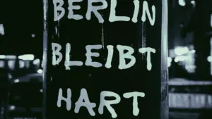 Schwarz-Weiß-Aufnahme eines Straßenschildes mit der Aufschrift 'Berlin bleibt hart' im nächtlichen Licht.