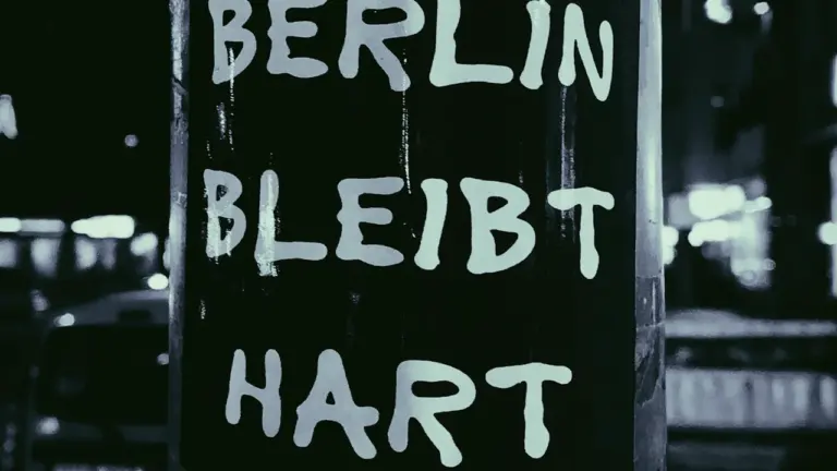 Schwarz-Weiß-Aufnahme eines Straßenschildes mit der Aufschrift 'Berlin bleibt hart' im nächtlichen Licht.