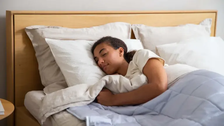 Eine junge Frau schläft friedlich in einem Bett mit hellen, neutralen Bettbezügen.