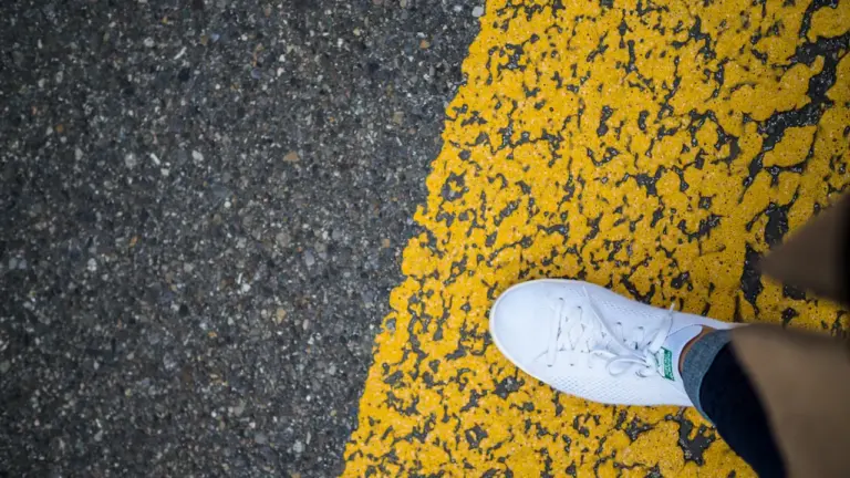 Ein einzelner weißer Sneaker steht auf dem Asphalt vor einer gelben Markierung.