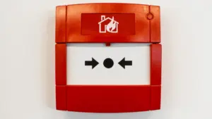 Roter Feuermelder mit Brandschutz-Symbol an einer weißen Wand im Innenbereich montiert.