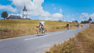 Radfahrer auf einer Landstraße vor einer Kirche bei strahlendem Sonnenschein.