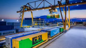 Ein Portalkran verlädt Container auf einen Güterzug während der Abenddämmerung im Industriehafen.