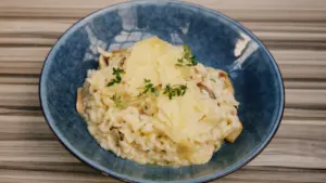 Ein blauer Teller mit cremigem Pilz-Risotto, garniert mit frischen Kräutern und Parmesan.