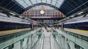 Ein Zug fährt in einen Bahnhof ein, im Hintergrund eine große Bahnhofsuhr sichtbar.