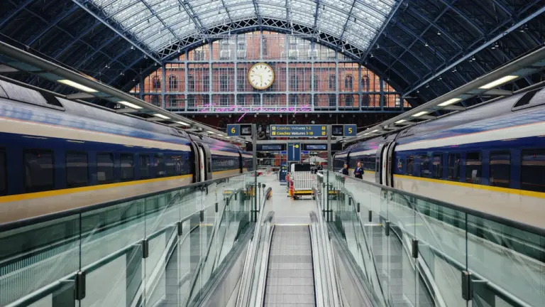 Ein Zug fährt in einen Bahnhof ein, im Hintergrund eine große Bahnhofsuhr sichtbar.