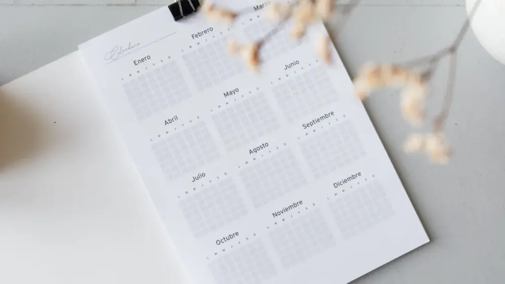 Ein offener Jahreskalender auf einem Schreibtisch mit Kaffee und Büroklammern zur Zeitplanung.