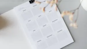 Ein offener Jahreskalender auf einem Schreibtisch mit Kaffee und Büroklammern zur Zeitplanung.