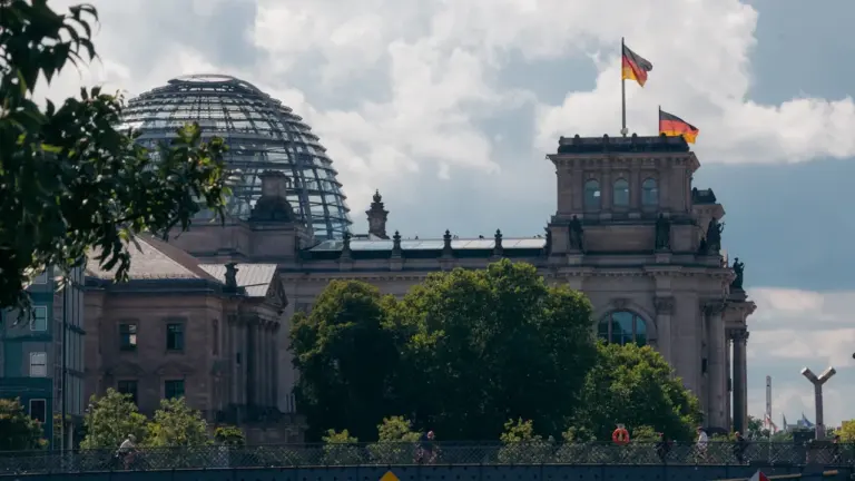 Das Reichstagsgebäude in Berlin mit wehenden deutschen Flaggen bei klarem Sommerwetter.