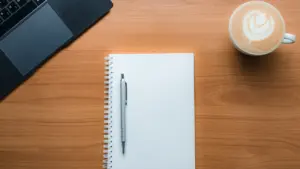 Ein Notizbuch mit Stift und eine Tasse Kaffee auf einem Holztisch.